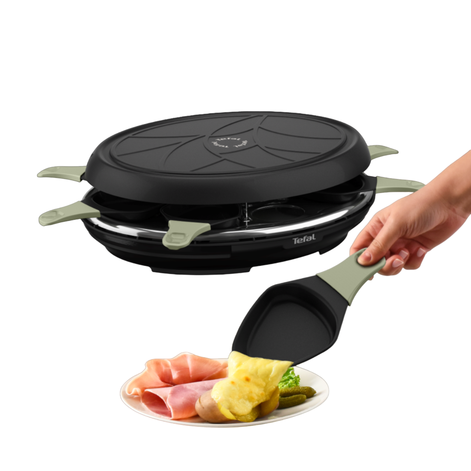 Raclette grill with food: ham, cheese, potatoes, and pickles on a plate. A hand holds a spatula.
