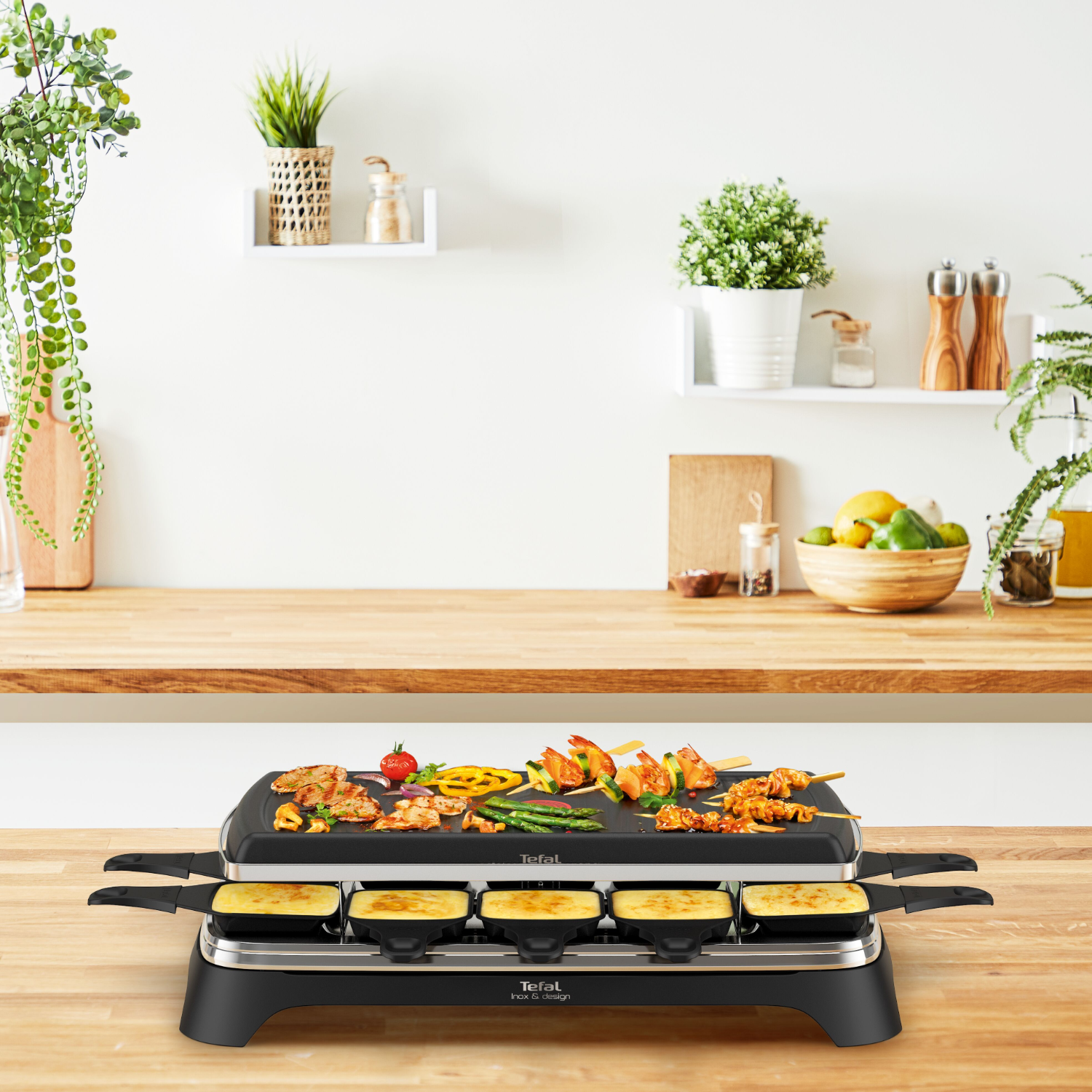 Raclette grill met eten erop. Keukenachtergrond met planten en planken.