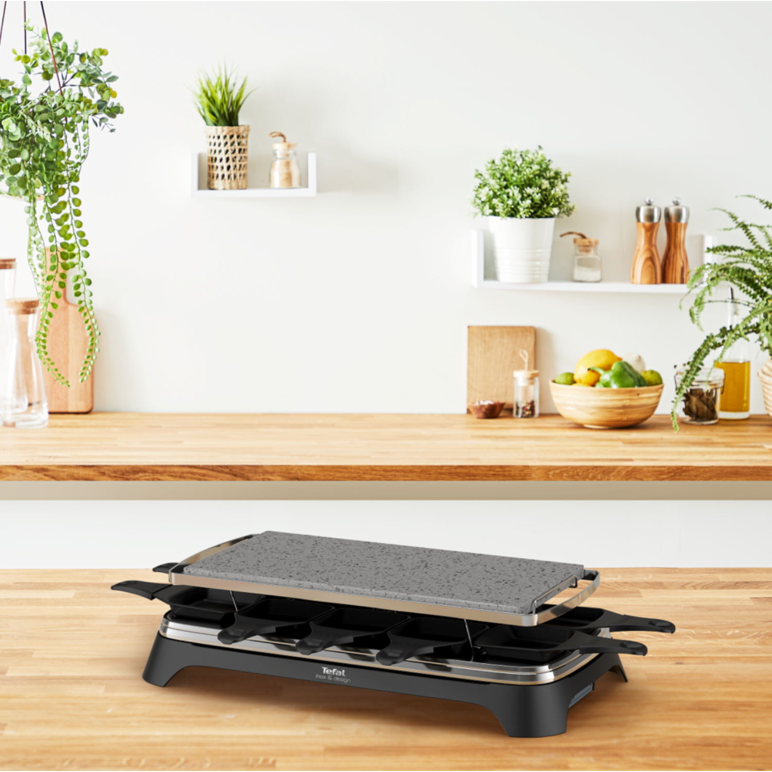 Raclette grill op een houten aanrecht, met planten en een houten achtergrond.