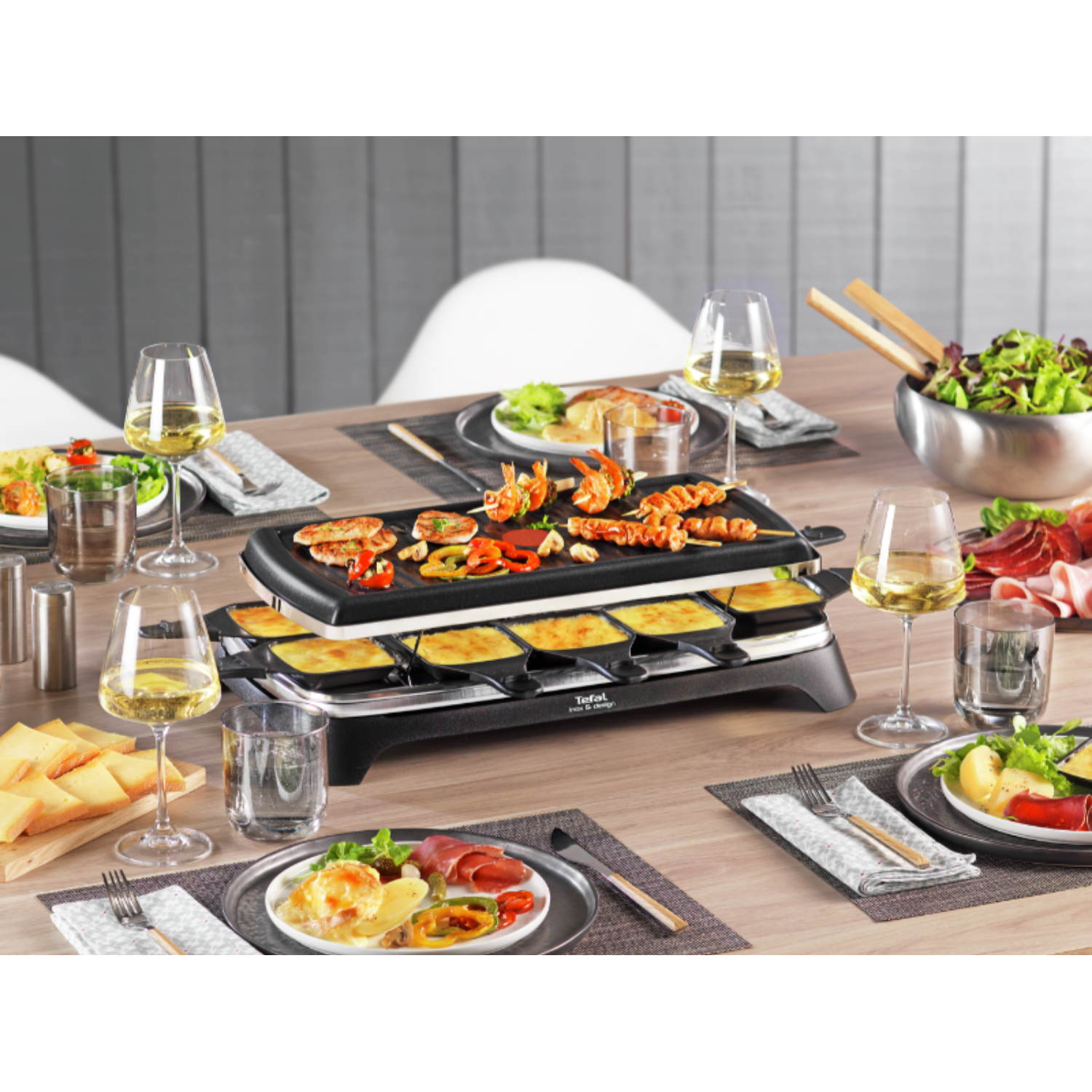 Une table dressée pour un repas. Grill à raclette au centre, avec nourriture, vin et assiettes.