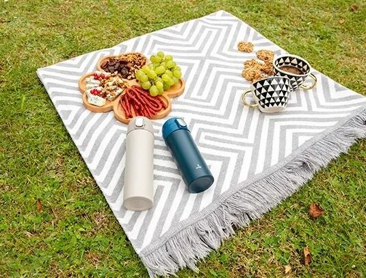 Ustawienie piknikowe na szaro-białym kocu z jedzeniem i dwiema butelkami wody.