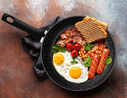 Patelnia z jajkami sadzonymi, boczkiem, pomidorami, fasolą, kiełbaskami i tostami.