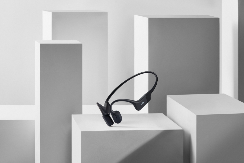 Casque à conduction osseuse sans fil, noir, posé sur des formes géométriques blanches.