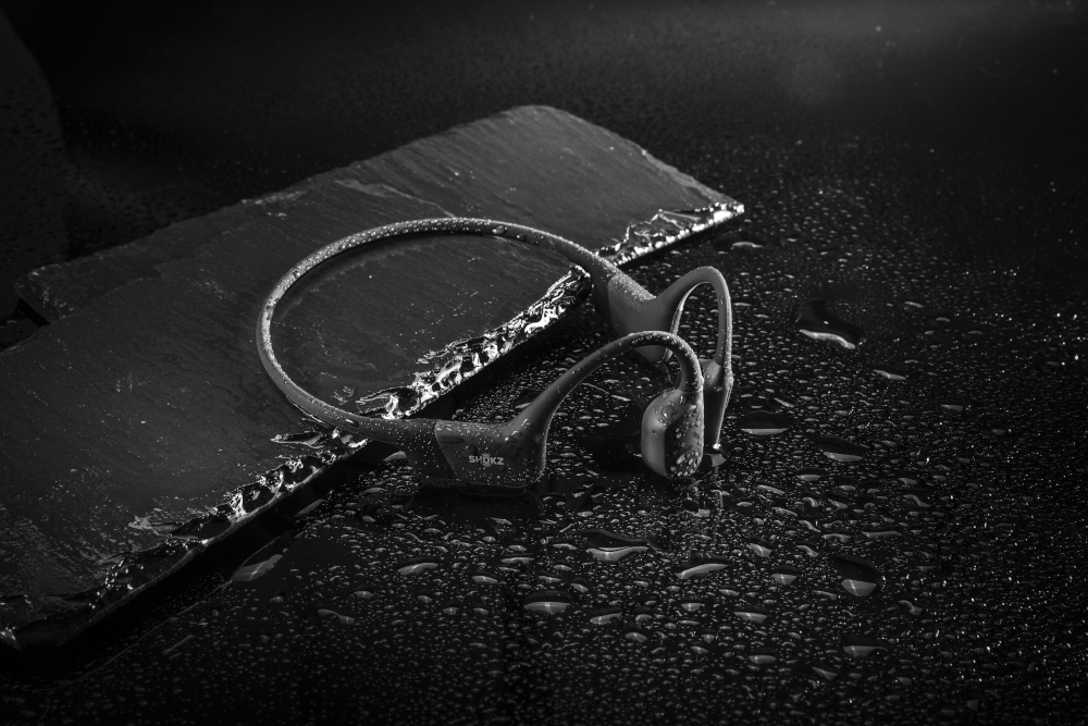 Image en noir et blanc d'écouteurs à conduction osseuse sur une surface sombre et mouillée.