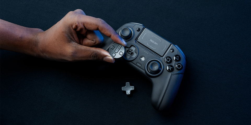Una mano sosteniendo un mando de juegos negro, con un D-pad que se coloca sobre él. Fondo oscuro.