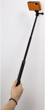 Ręka osoby trzymającej kij do selfie z dołączonym pomarańczowym aparatem.