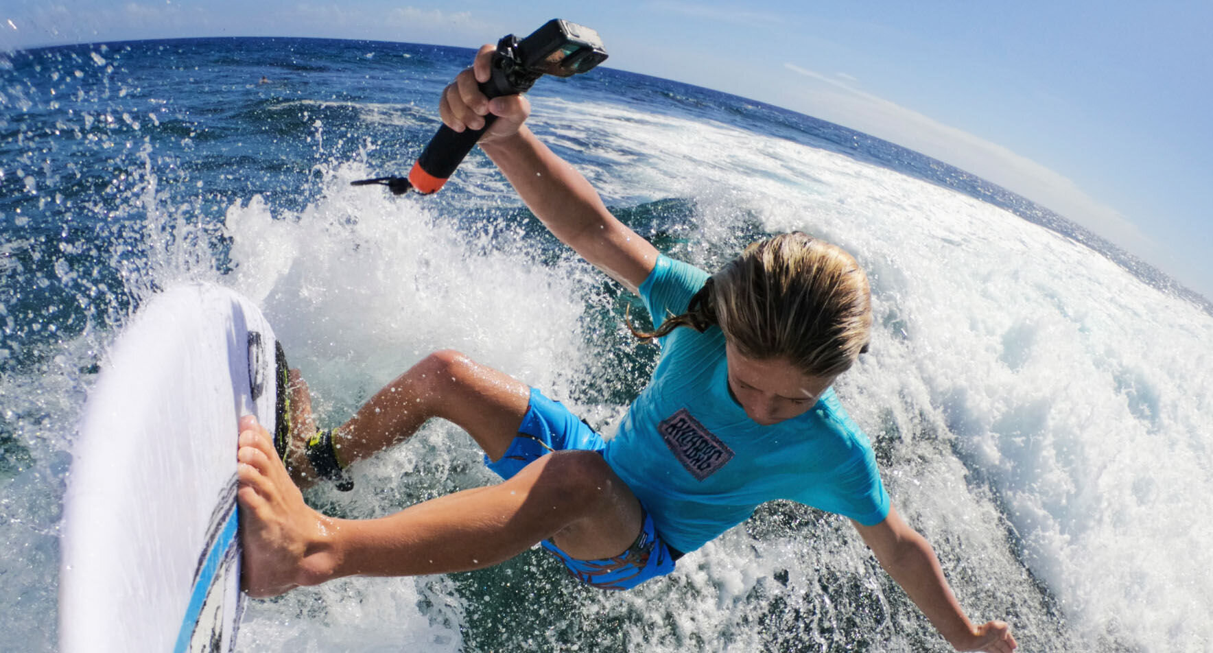 Młody surfer na fali. Trzyma kamerę i jedzie na desce surfingowej.