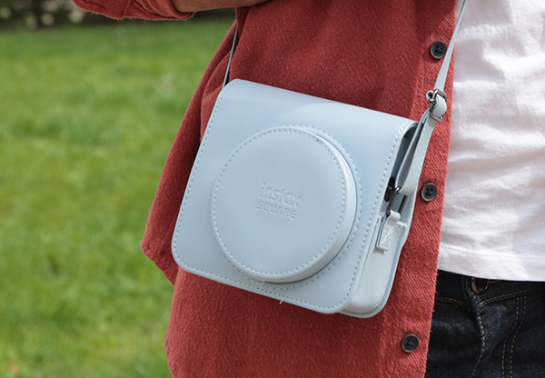 Osoba trzymająca jasnoniebieski futerał na aparat z paskiem na ramię.