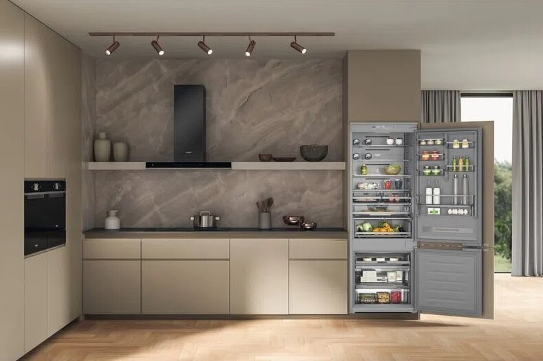 Nowoczesna kuchnia z otwartą lodówką. Kuchnia ma marmurową ścianę i beżowe szafki. Są światła.