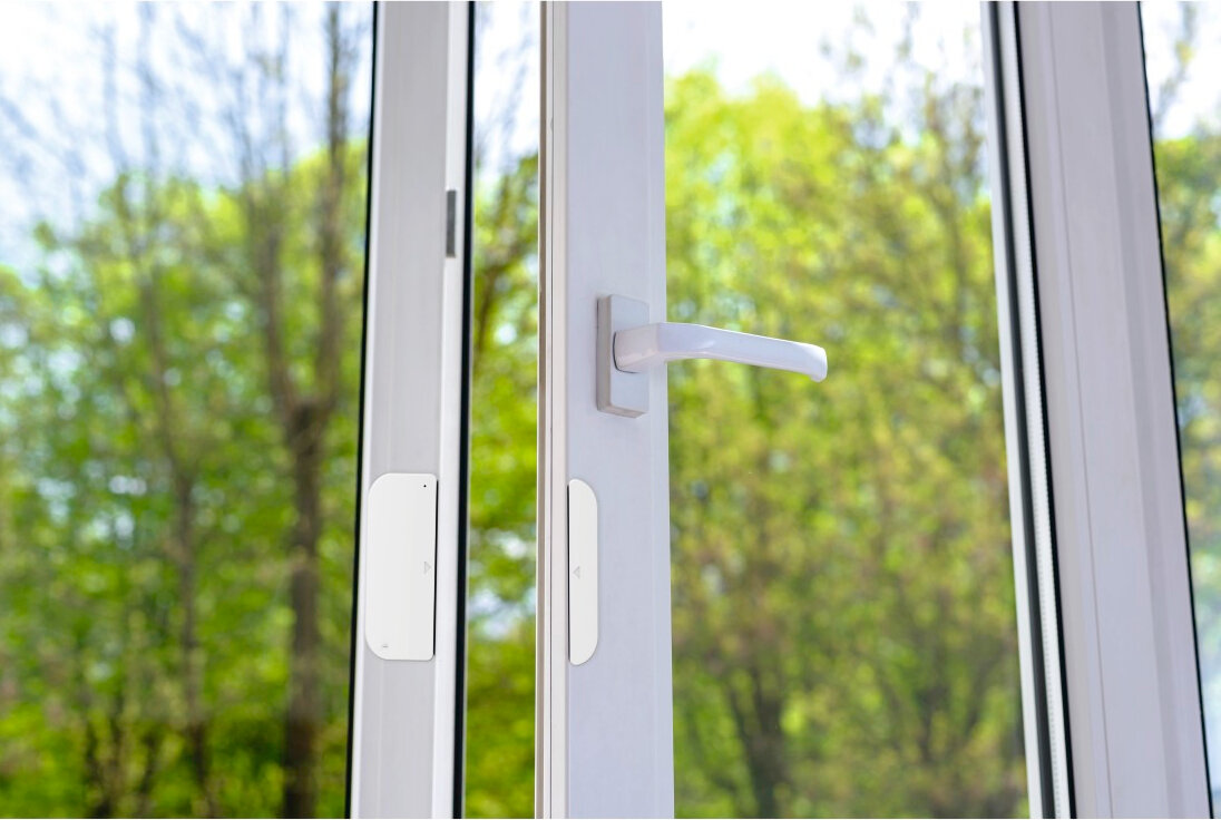 Biała okno z ramą, z uchwytem i widokiem na zielone drzewa.