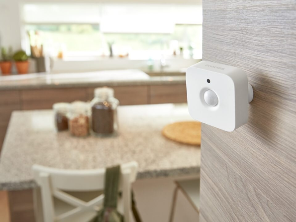 Biały czujnik ruchu Philips Hue zamontowany na drewnianej ścianie w kuchni.