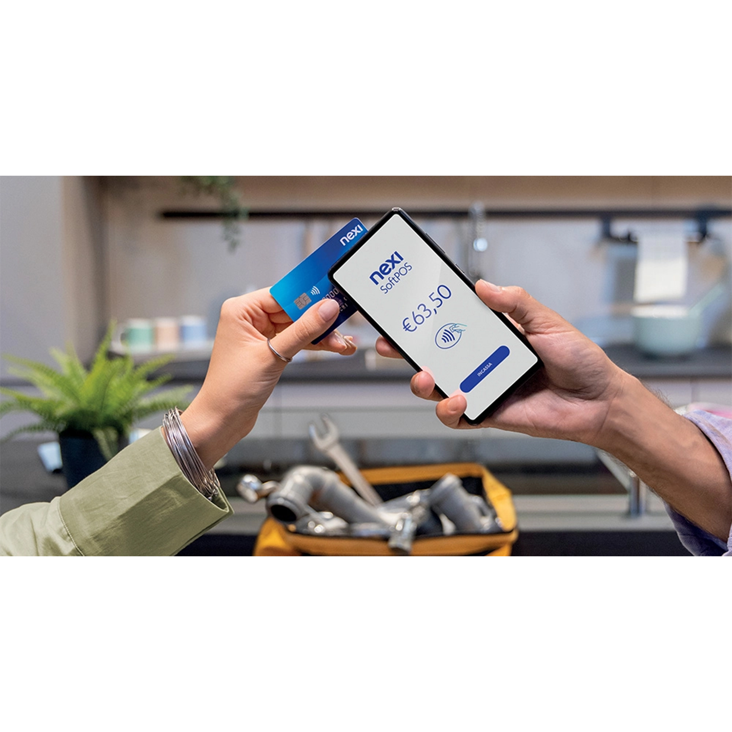 Mani che tengono una carta di credito e un telefono con un display Nexi SoftPOS. Pagamento in corso.