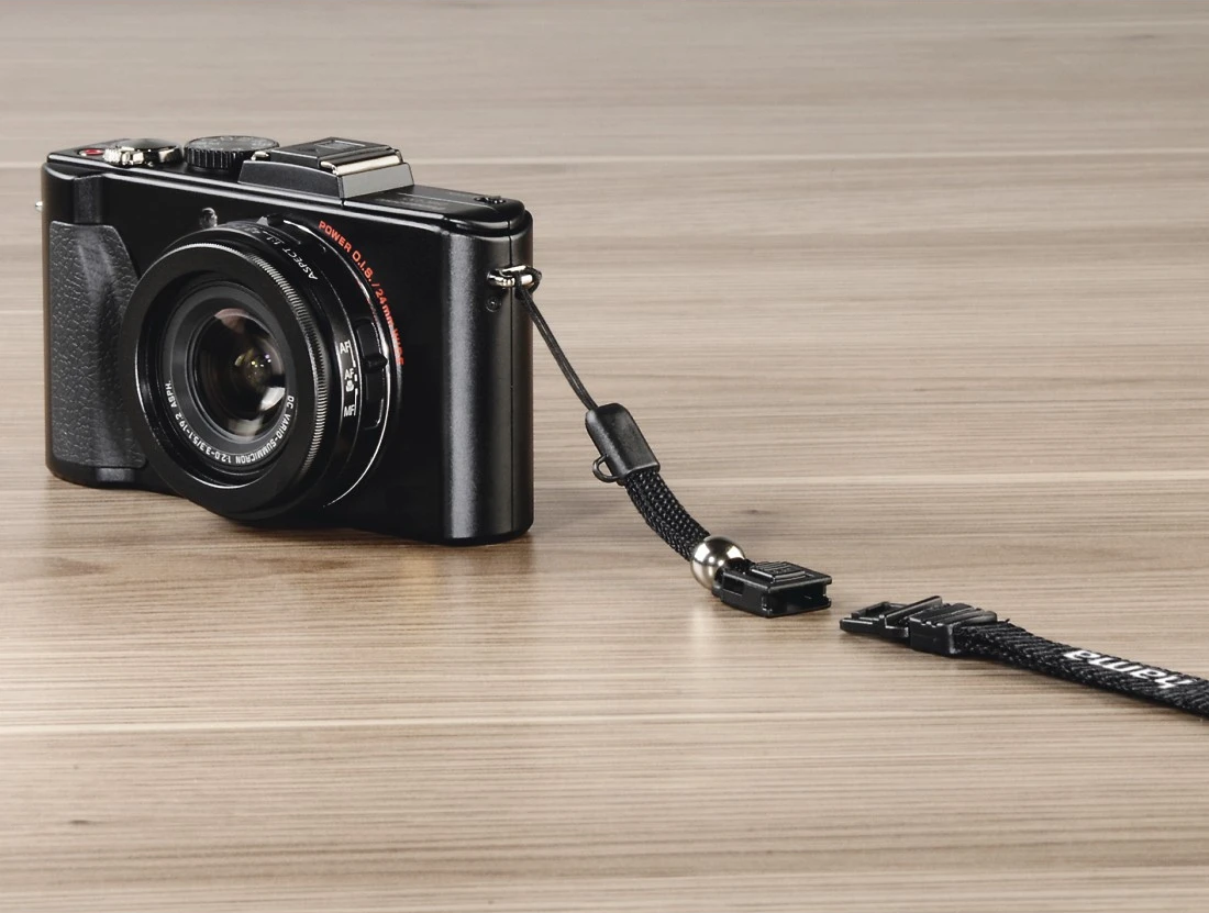 Un appareil photo noir avec une sangle, posé sur une surface en bois, avec la sangle détachée.