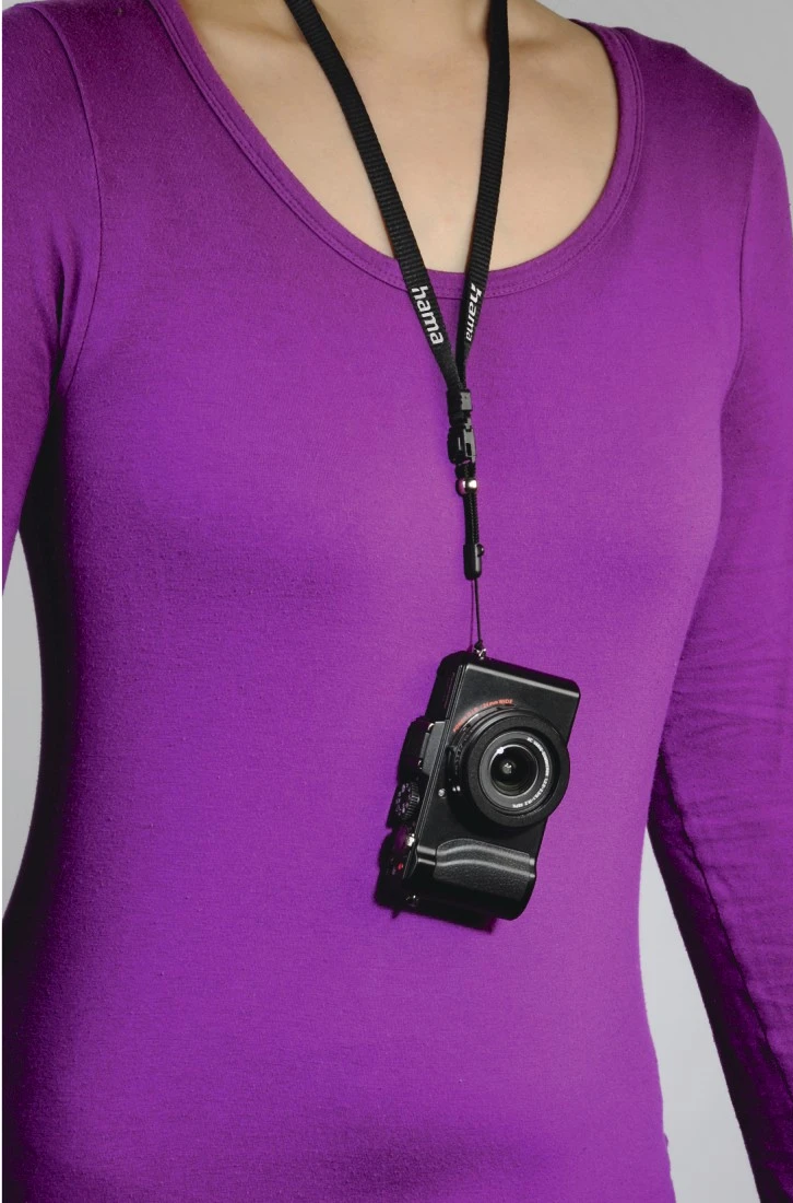 Une personne portant une chemise violette a un appareil photo suspendu à son cou sur une sangle noire.