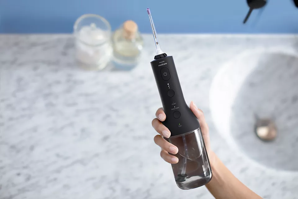 Un idropulsore nero e argento tenuto in mano. Bagno sullo sfondo.