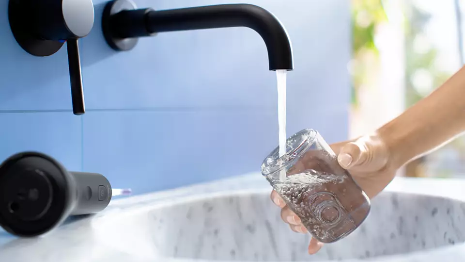 L'acqua scorre da un rubinetto nero in un bicchiere. Un irrigatore orale nero a sinistra.