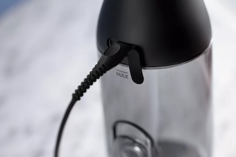 Primo piano di una bottiglia d'acqua nera con un cavo di ricarica inserito e un marchio 'MAX'.