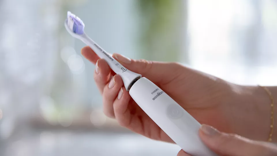 Una persona tiene in mano uno spazzolino elettrico bianco. La testina è viola e bianca.