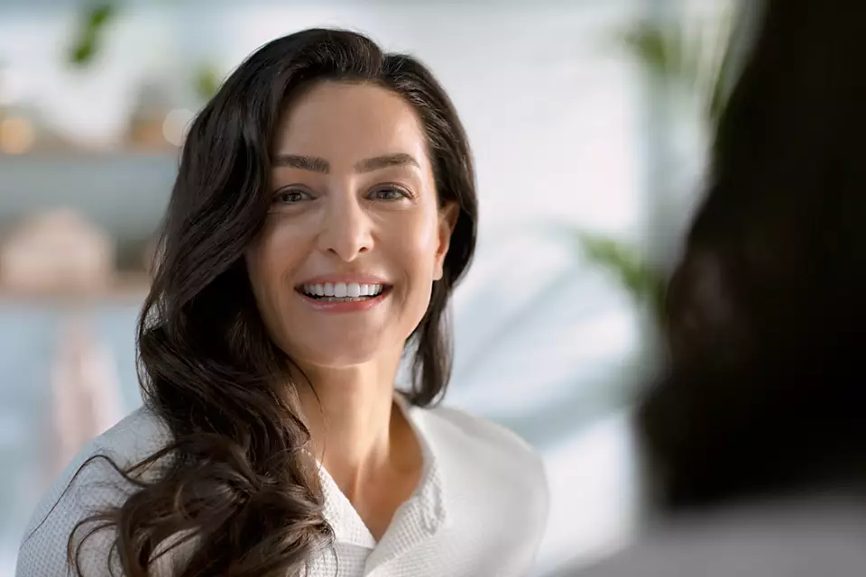 Donna sorridente in accappatoio bianco, capelli scuri lunghi, guarda la fotocamera.