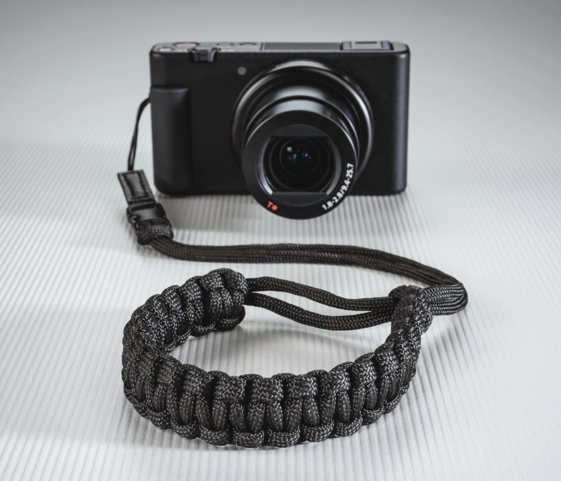 Un appareil photo noir avec une dragonne. La dragonne est en cordon tressé noir.