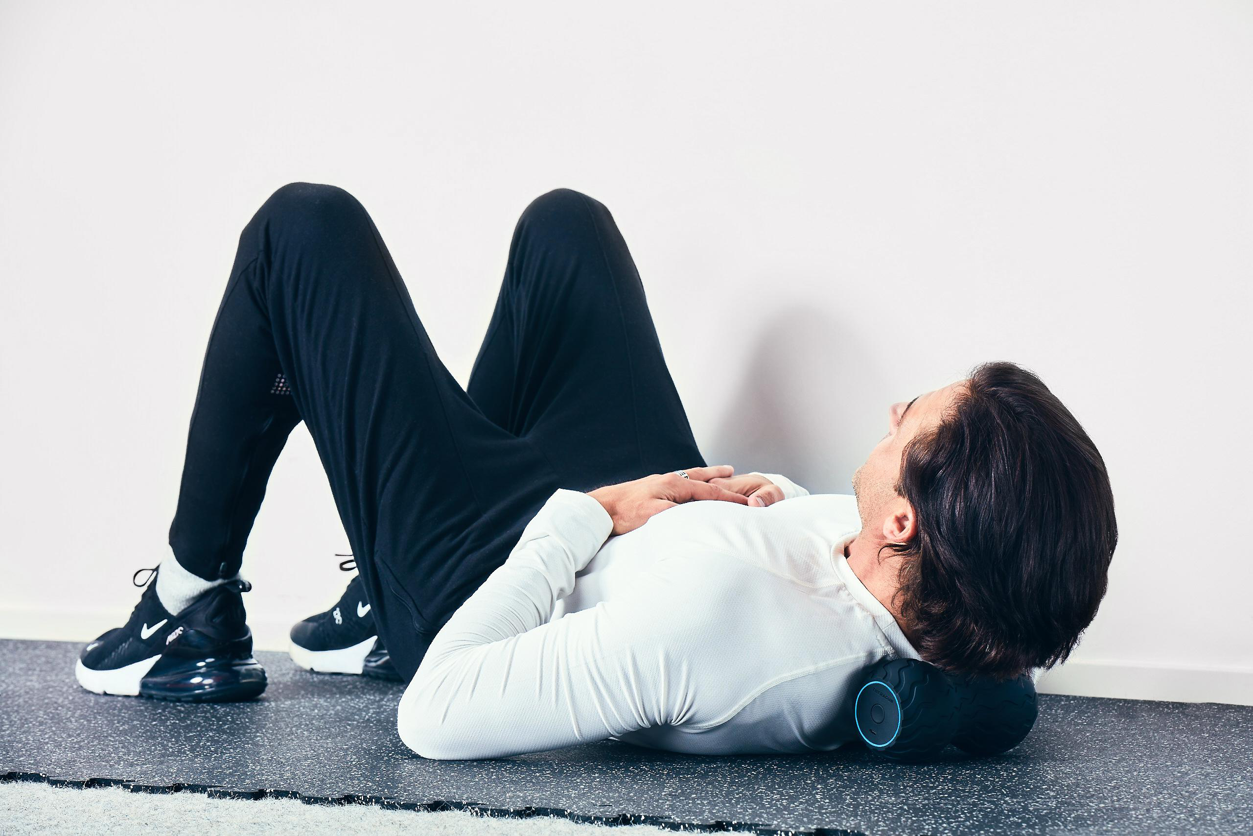 Ein Mann liegt auf dem Boden mit einer schwarzen Massagerolle unter dem Nacken.