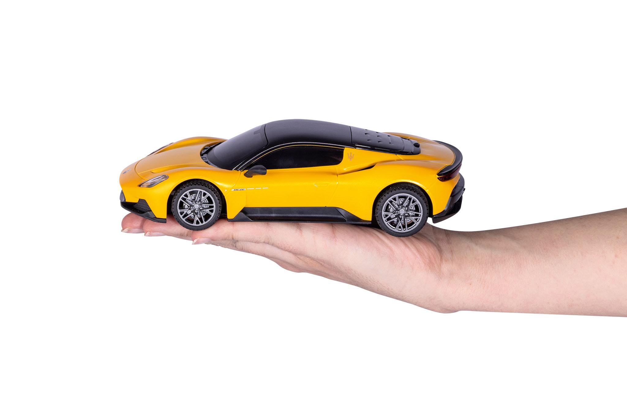 Ein gelbes Spielzeugauto, das in einer Hand gehalten wird, mit schwarzem Dach, vor weißem Hintergrund.