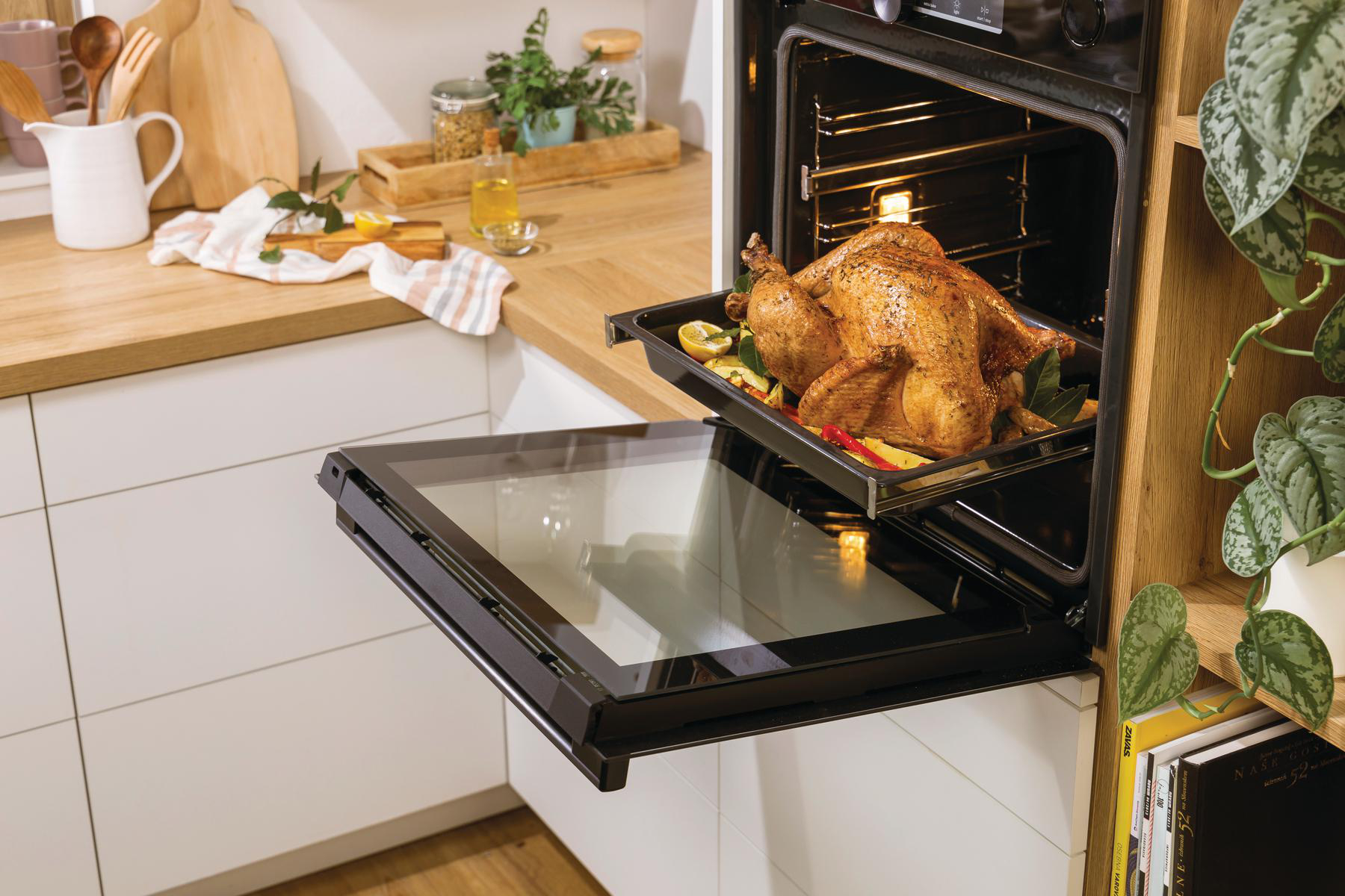 Ofen mit gebratenem Huhn auf einem Blech. Offene Backofentür, Kücheninterieur, Holztisch sichtbar.