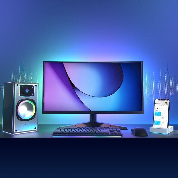 Konfiguracja komputera z monitorem, głośnikiem, klawiaturą, myszką i telefonem na biurku. Niebieskie i fioletowe oświetlenie.