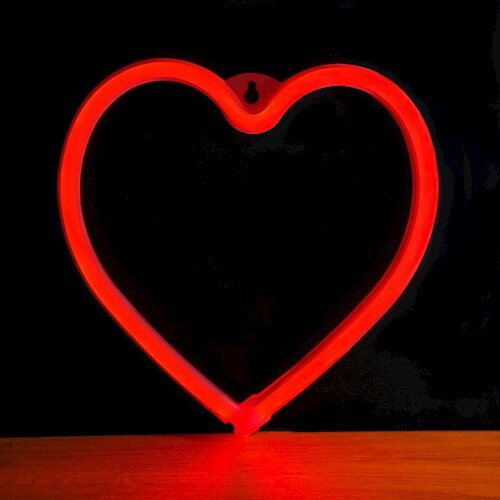 Czerwone neonowe serce na czarnym tle, na drewnianej powierzchni.
