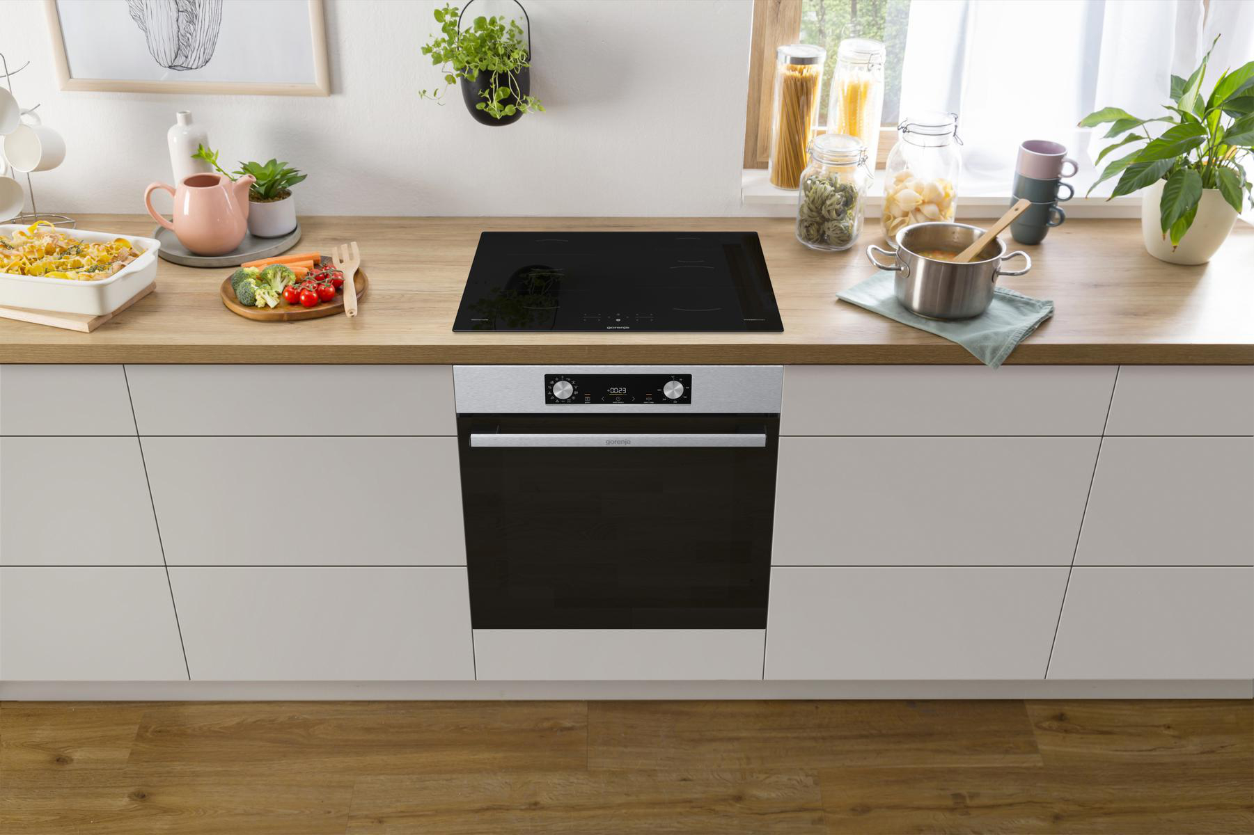 Moderne Küchenszene mit Induktionskochfeld auf Holztresen, Backofen darunter und Pflanzen.