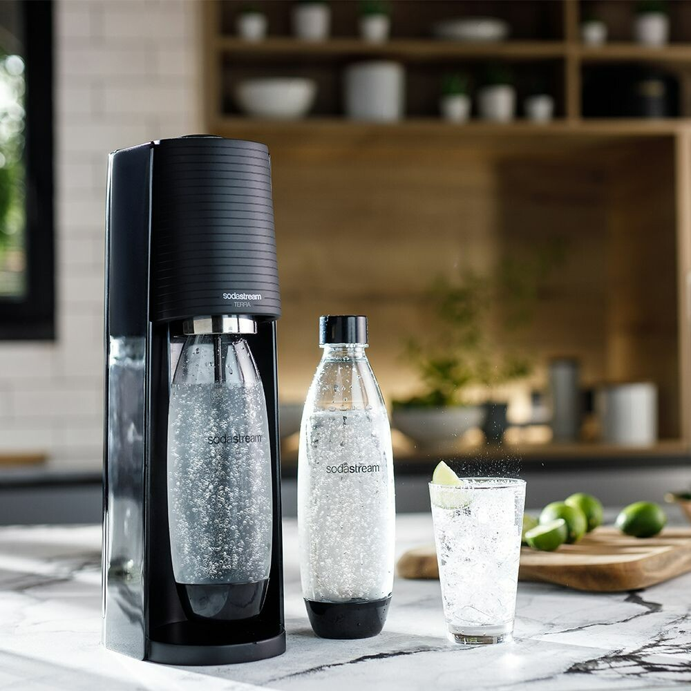 SodaStream gép két palackkal. Az egyik a gépen, a másik egy pohár közelében.