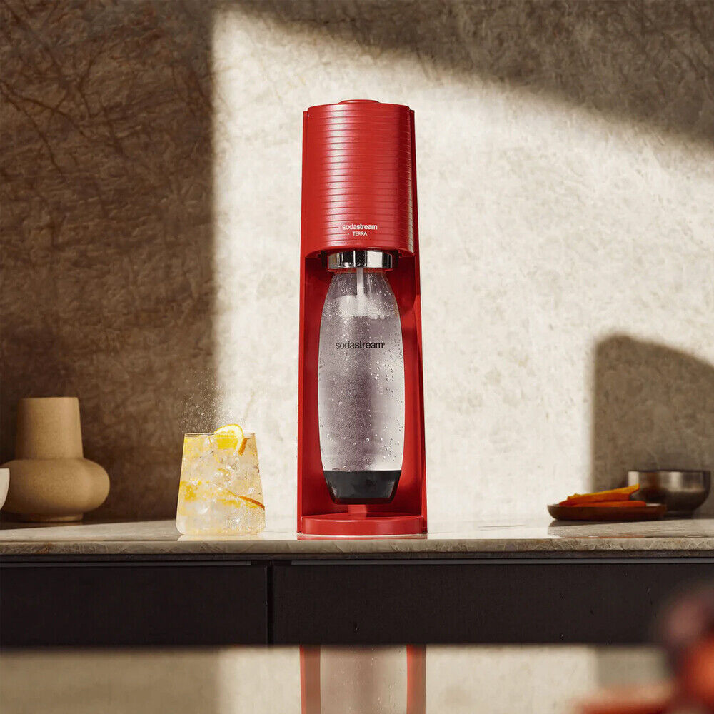 Piros SodaStream gép egy pohár szénsavas vízzel és egy szelet citrommal.
