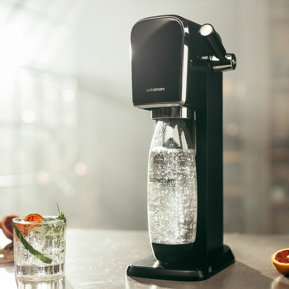 Egy fekete SodaStream gép palackkal és koktélpohárral.