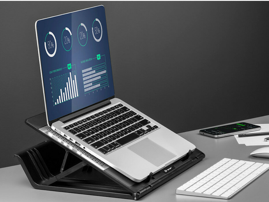 Laptop na stojaku wyświetla wykresy. Klawiatura i telefon są w tle.