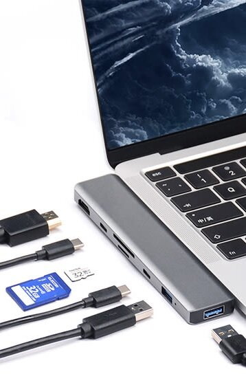 Srebrny hub do laptopa z różnymi portami, podłączony do laptopa. Kable, karta SD i USB.