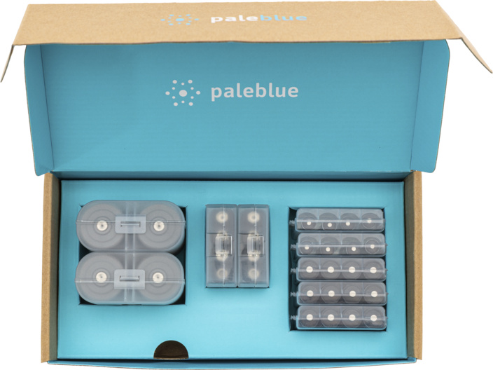 Scatola aperta con batterie. Batterie AA, AAA e C in custodie trasparenti, disposte all'interno blu e all'esterno in cartone marrone.