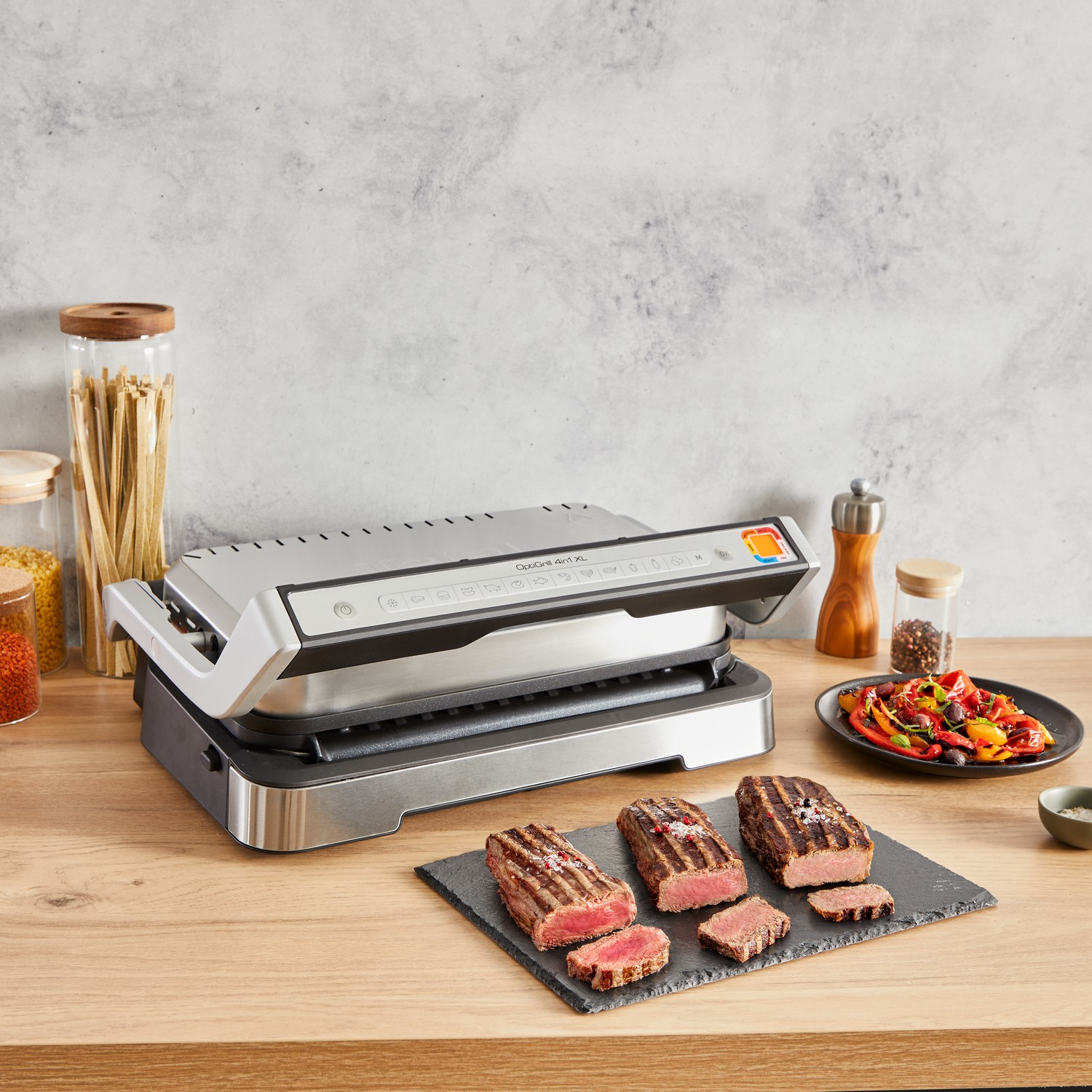 Een binnengrill met gebakken steaks, groenten en kruiden op een houten tafel.