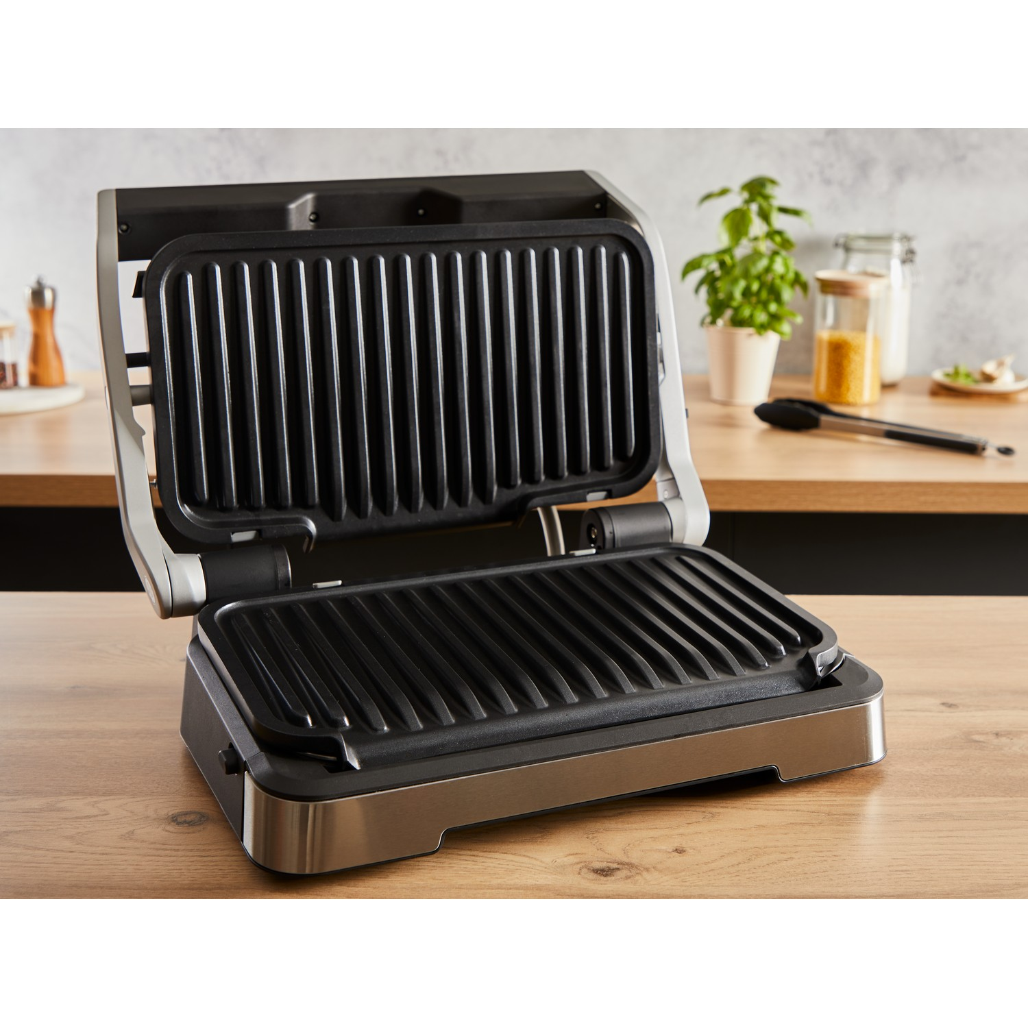 Een open zwarte grill met een roestvrijstalen basis, op een houten oppervlak.