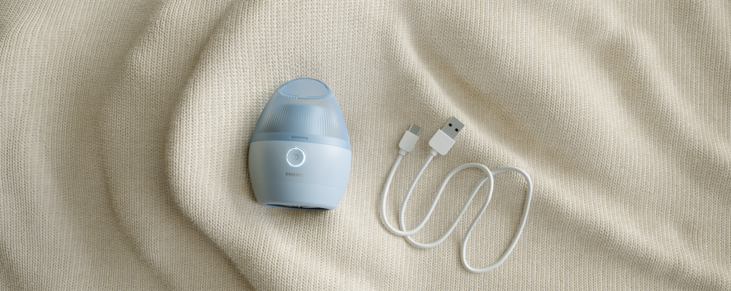 Cepillo de limpieza facial azul claro con cable de carga, sobre tela beige.