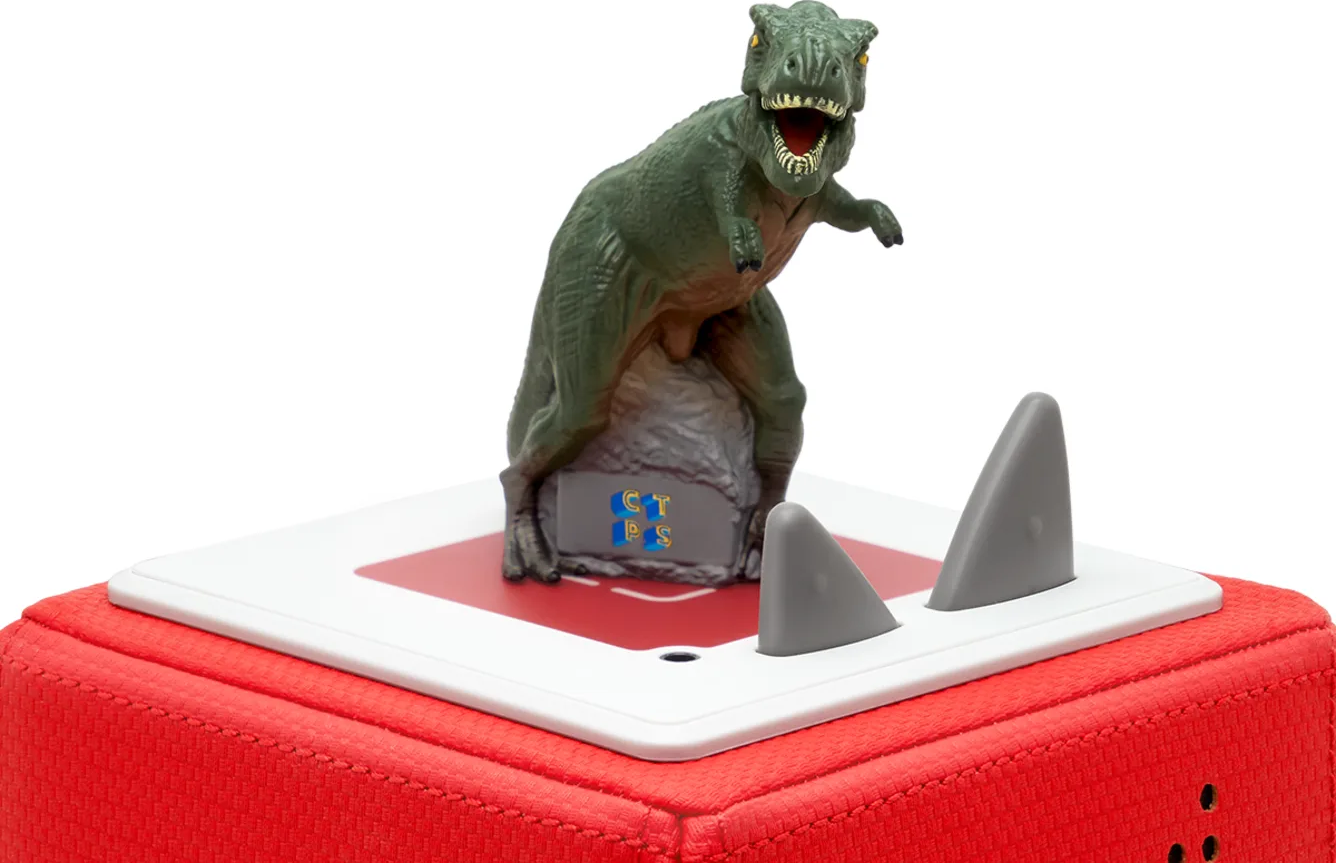 Spielzeug-Dinosaurier auf roter Basis mit weißer Oberseite. Zwei graue Flossen. Weißer Hintergrund.