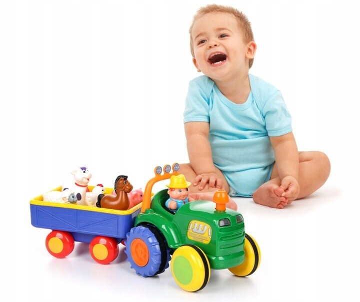 Mały chłopiec śmieje się obok zielonego traktora zabawki ciągnącego wózek z zabawkami zwierząt.