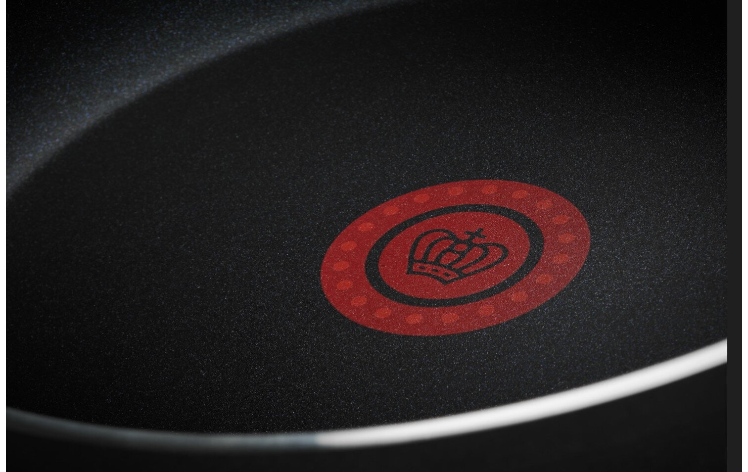 Zbliżenie czarnej patelni z czerwonym logo korony.