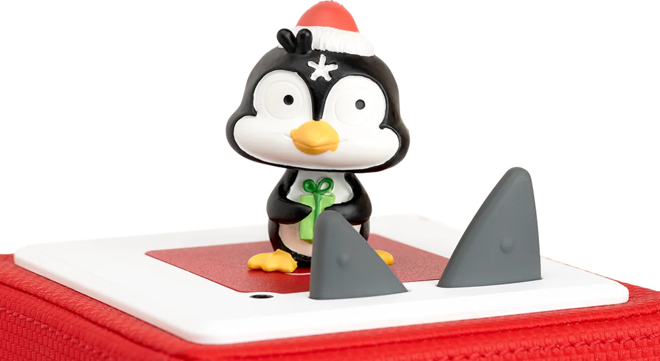Un jouet pingouin portant un chapeau de Père Noël, tenant un cadeau et des ailerons de requin.