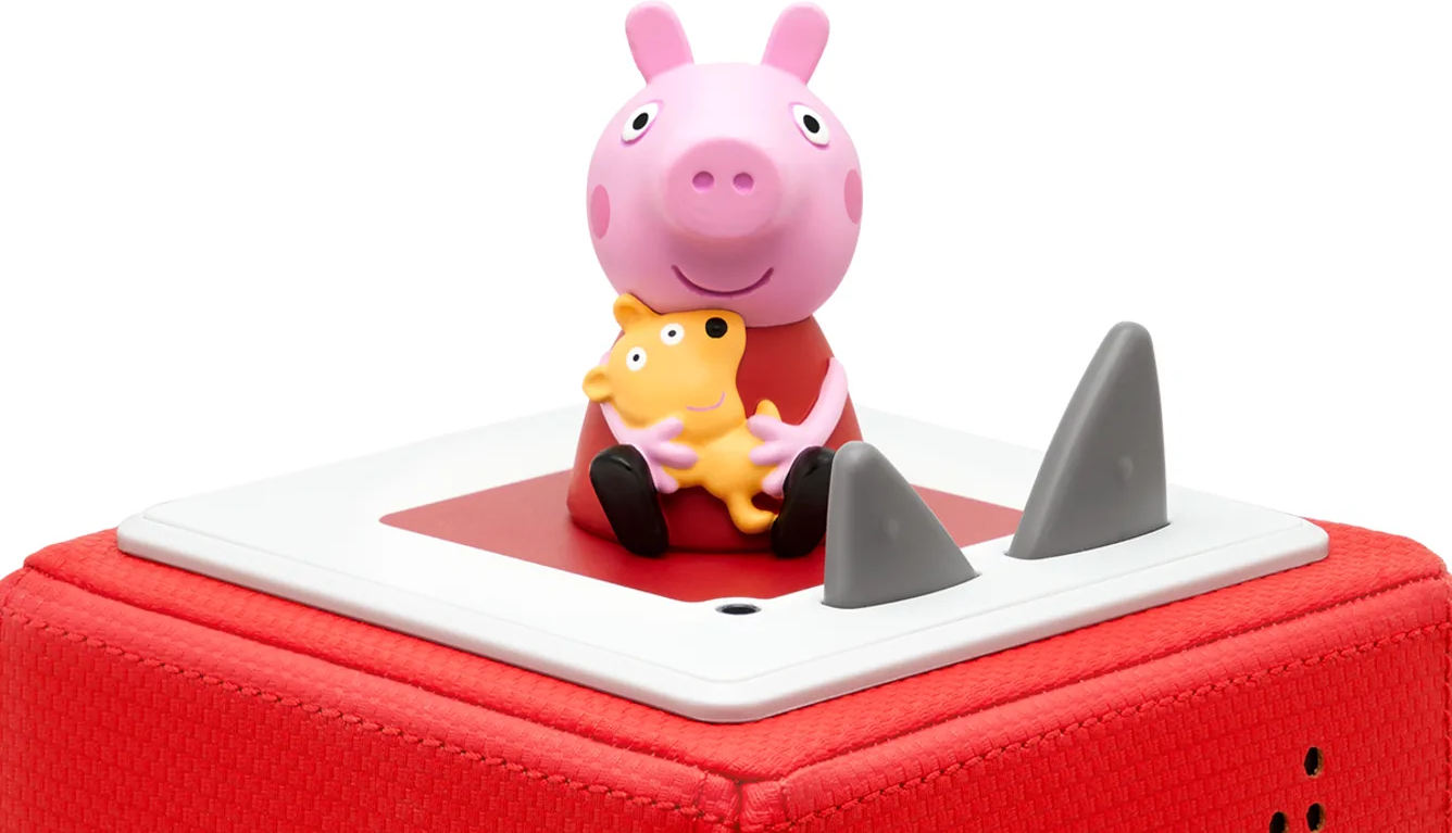 Peppa Wutz Figur, die einen gelben Bären auf einer roten Box mit Haifischflossen umarmt.