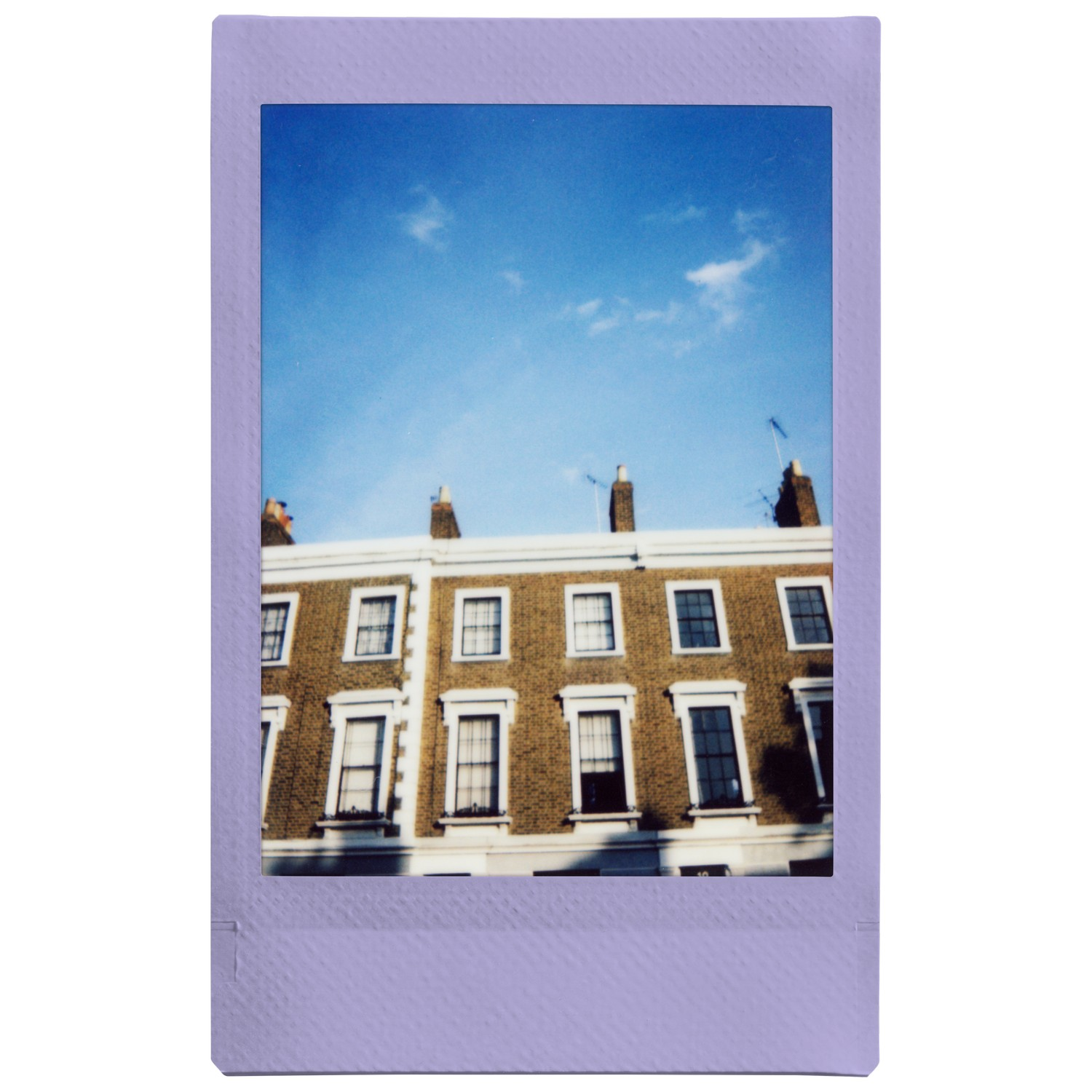 Un polaroïd encadré d'un immeuble en briques avec des fenêtres sous un ciel bleu.