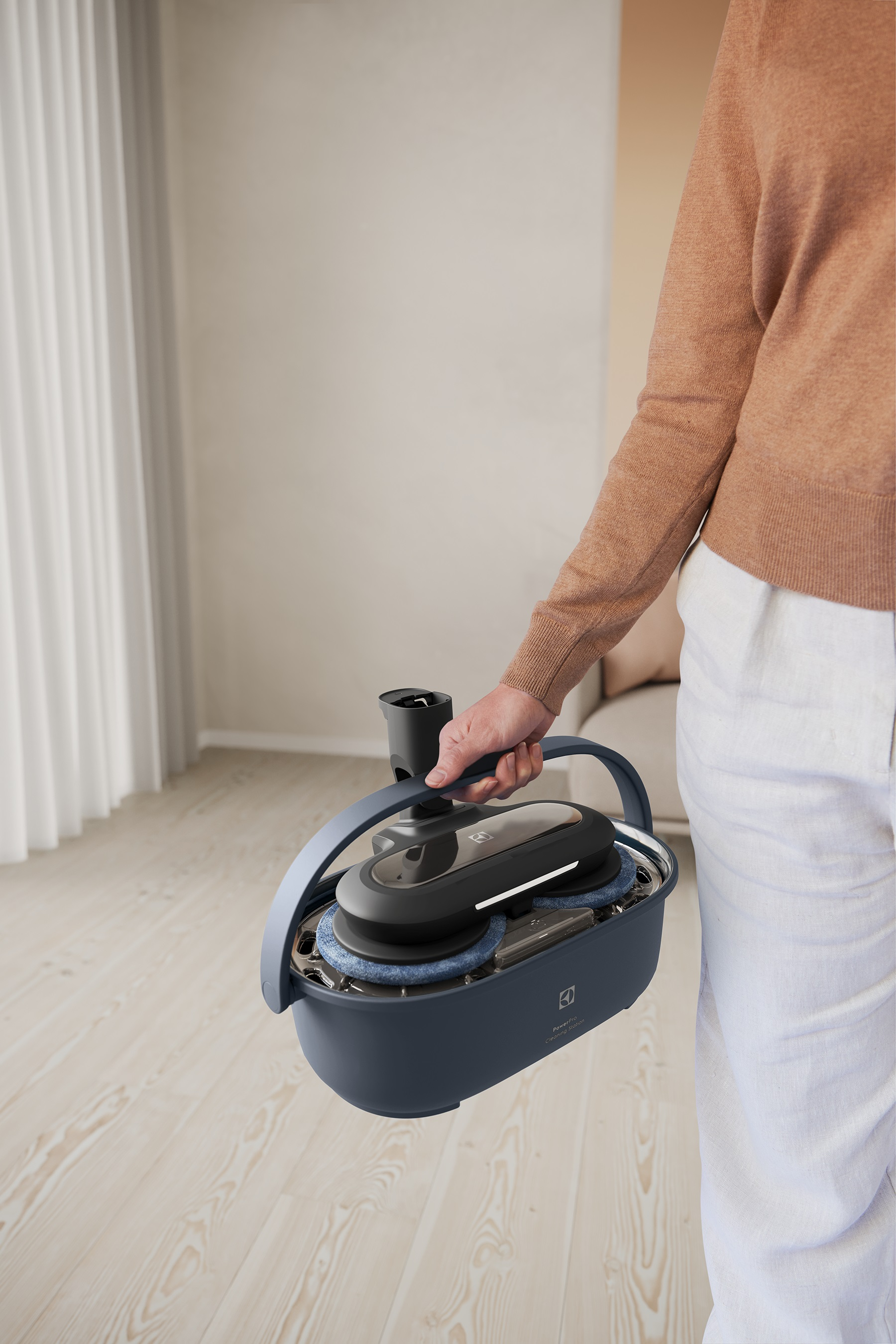 Bir kişi, bir tutma kolu ve tekerlekleri olan mavi ve siyah bir Electrolux zemin temizleyici tutuyor.