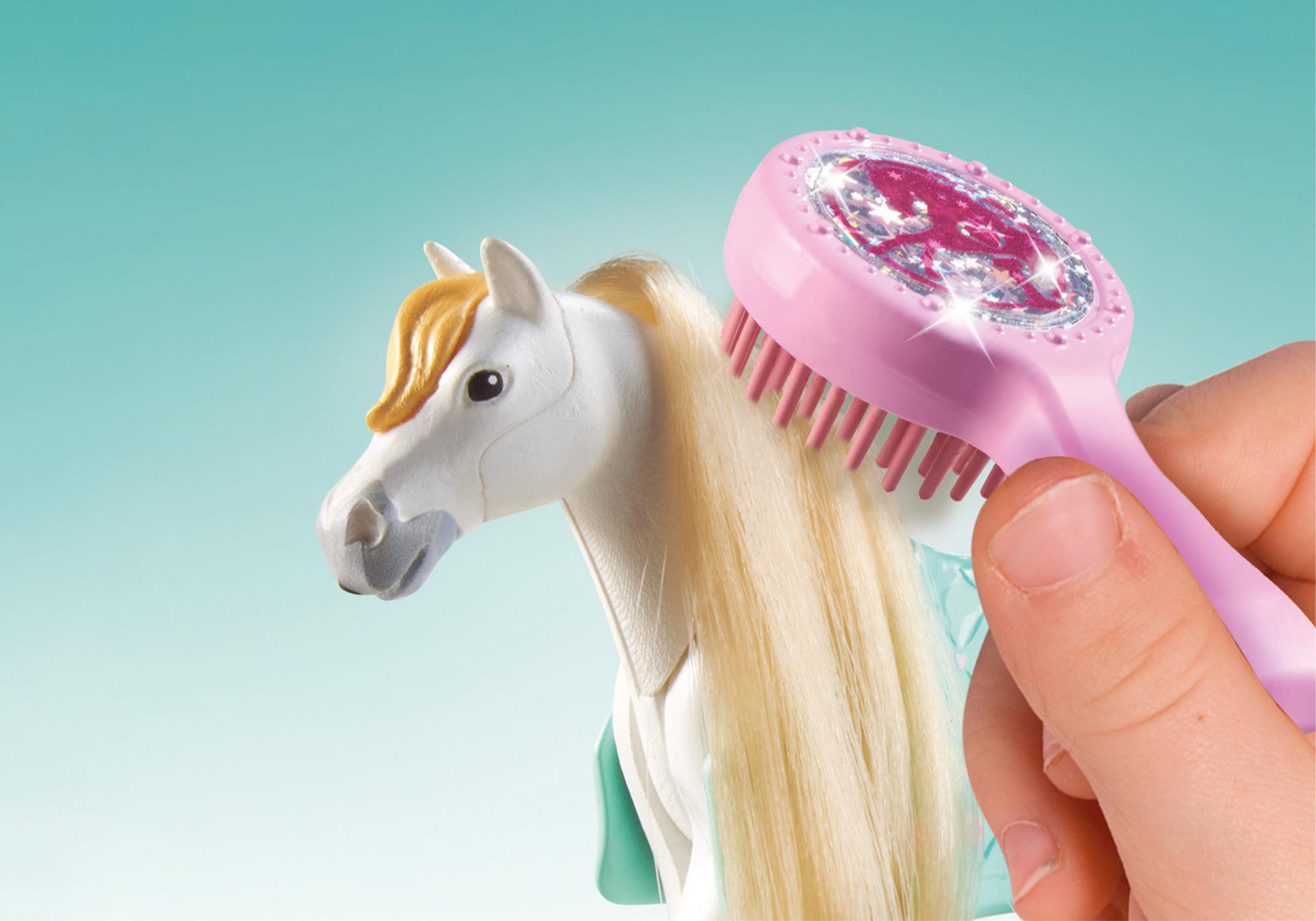 Eine Hand bürstet die blonde Mähne eines weißen Spielzeugpferdes mit einer rosa Bürste.