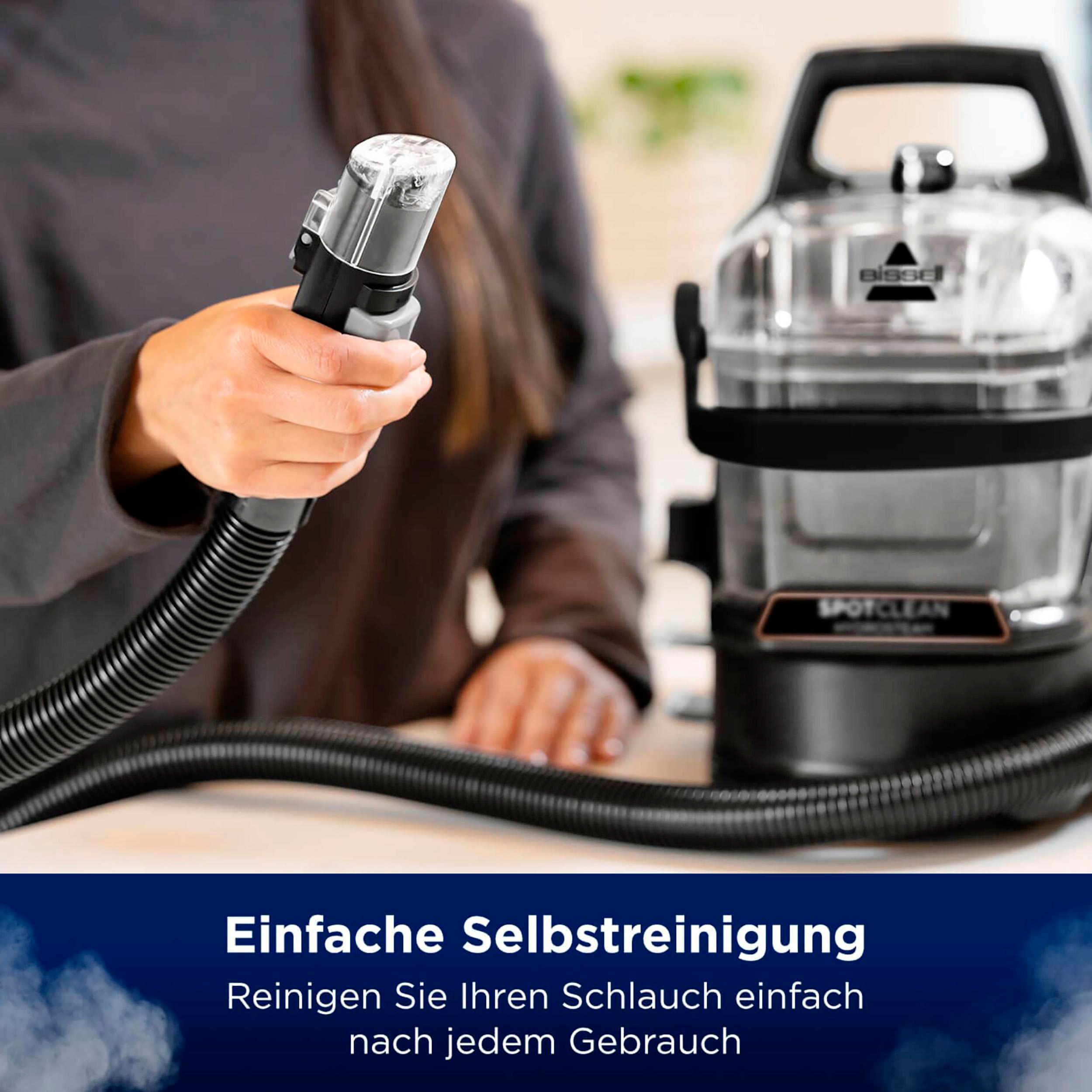 Eine Person hält ein Reinigungswerkzeug, das mit einem schwarzen Staubsauger verbunden ist.