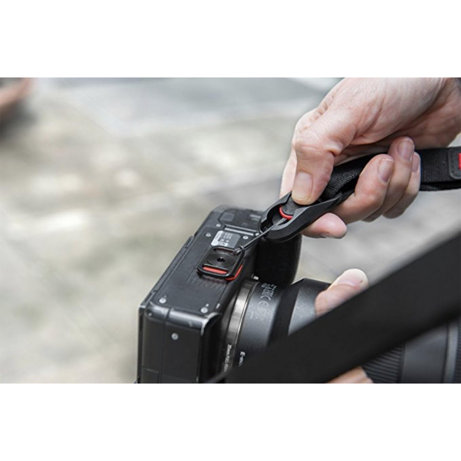 Mani di una persona che attacca una tracolla a una fotocamera. Primo piano.