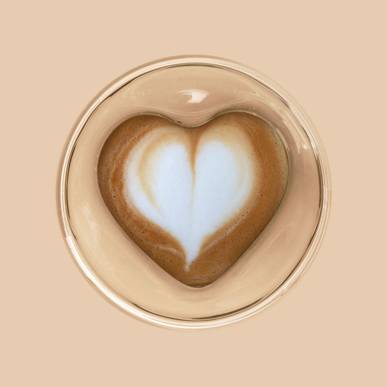 Latte art egy üvegpohárban. Szív alak a bézs háttéren.